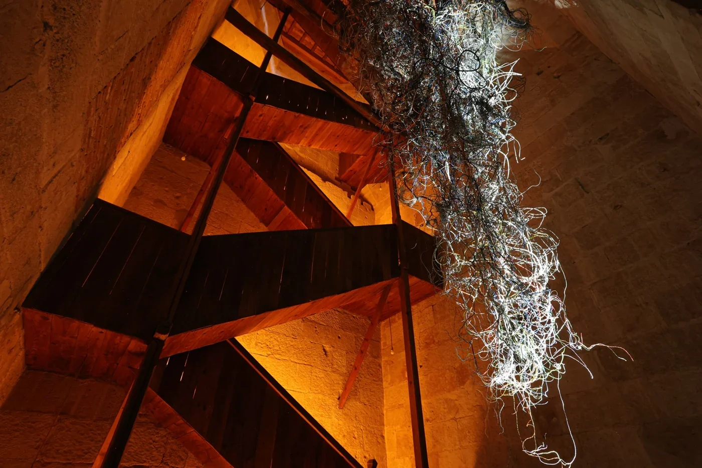 Enchevêtrement de câbles parcouru de lumière dans une charpente / Light travelling through tangled cables beneath timber beams.