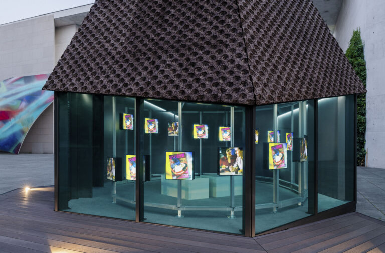 Vue extérieure du pavillon vitré de Peace Core (surround), avec plusieurs écrans lumineux à l’intérieur