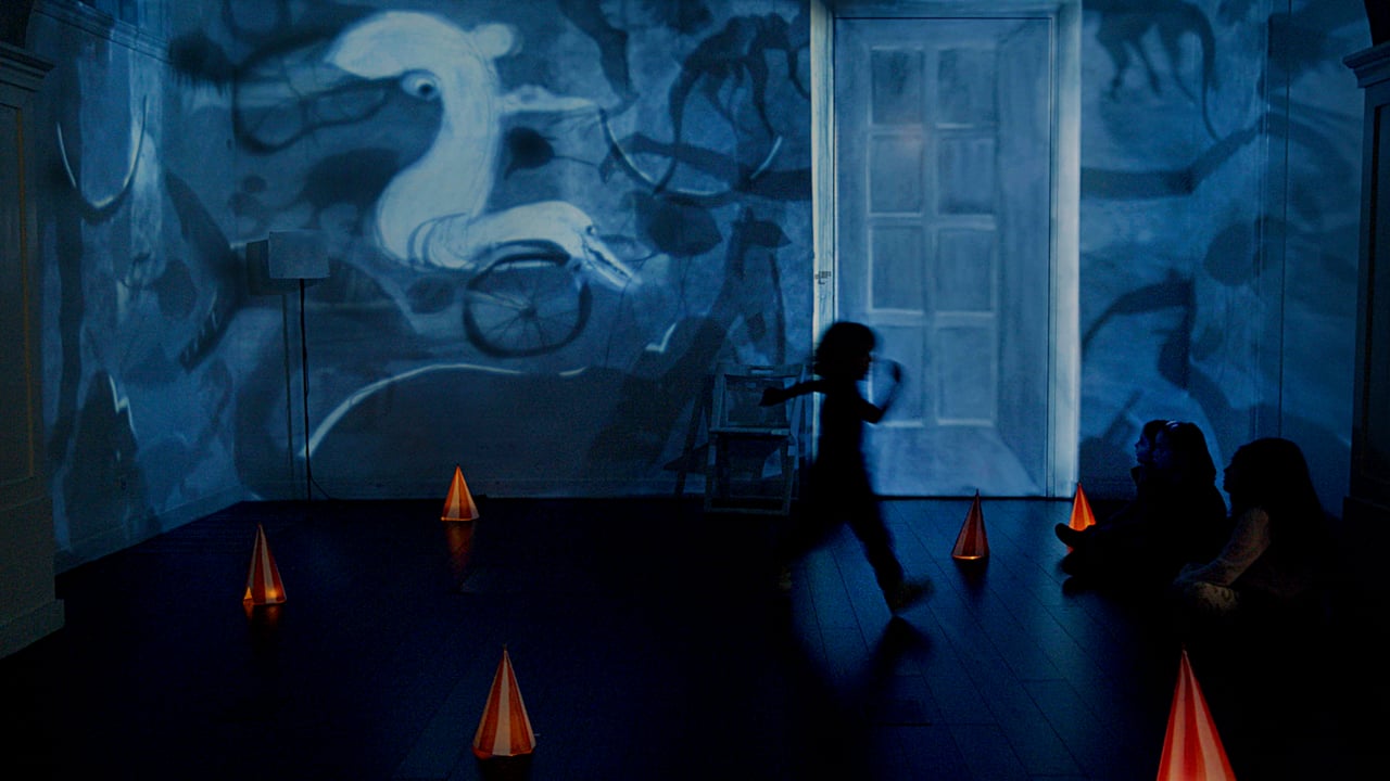 Une silhouette traverse une salle couverte de projections bleues, avec de petites formes orange au sol.