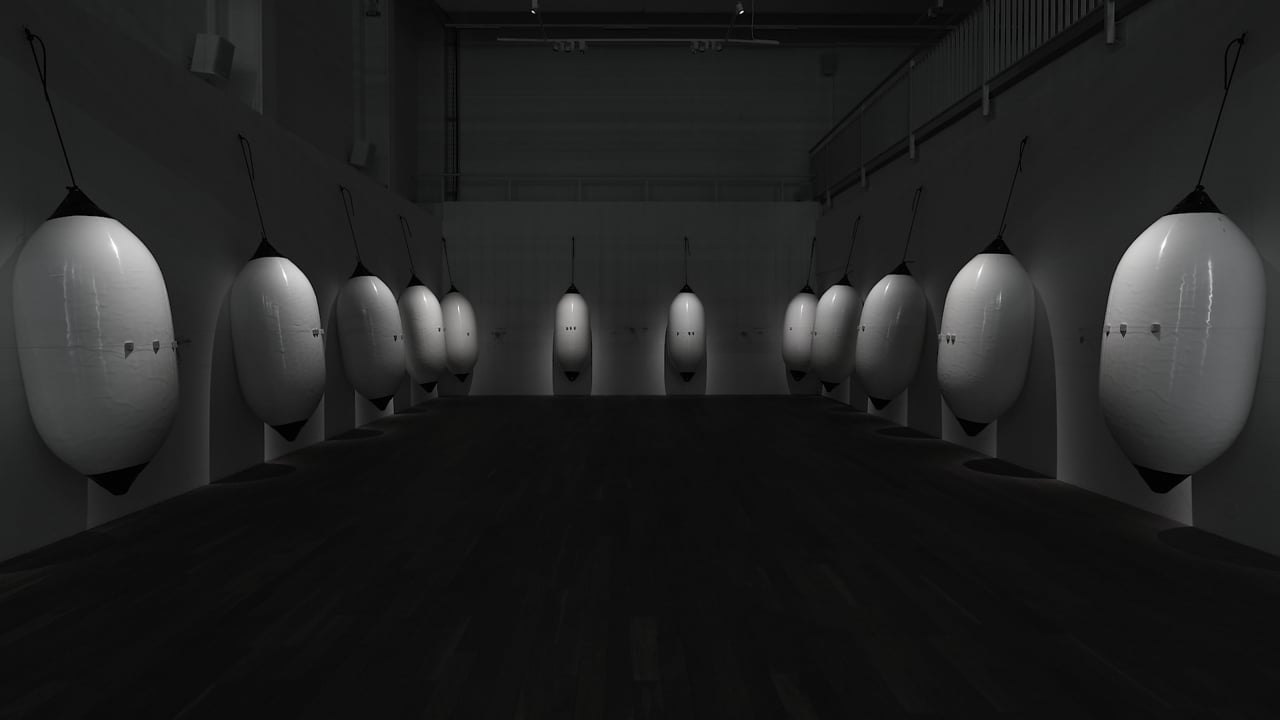 Douze grandes défenses de bateau suspendues dans une salle sombre.