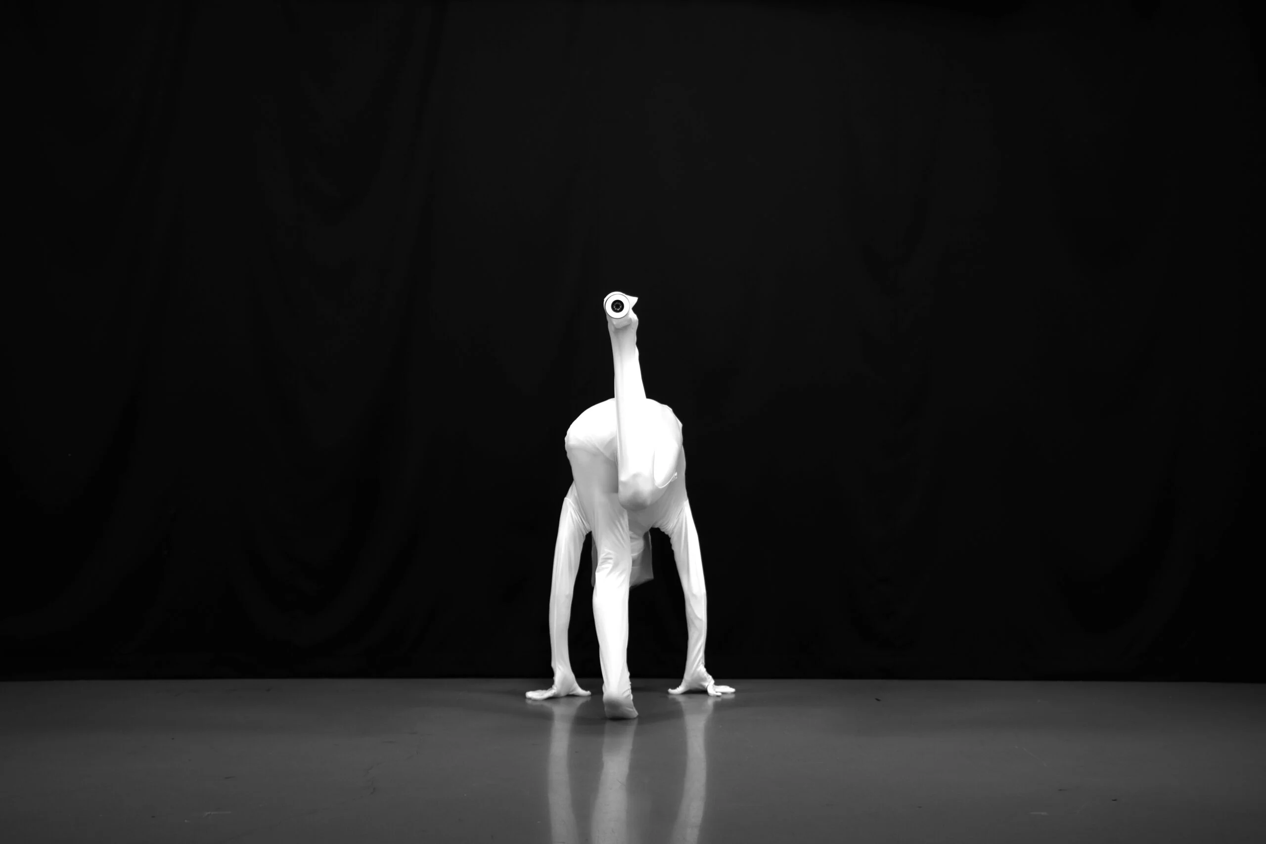 Figure en combinaison blanche, penchée sur ses mains, avec un dispositif optique sur un pied levé : CHIMERIA de Shin Hanagata.
