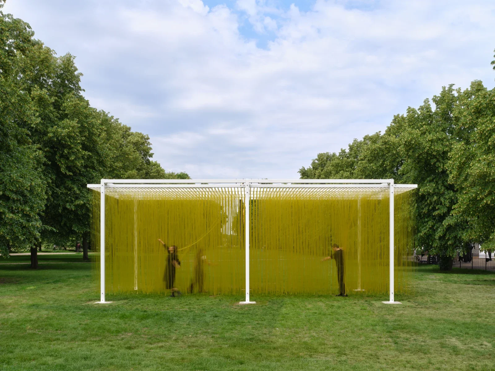 Des visiteurs traversent les tubes jaunes suspendus de Pénétrable BBL Jaune dans les jardins de Kensington.