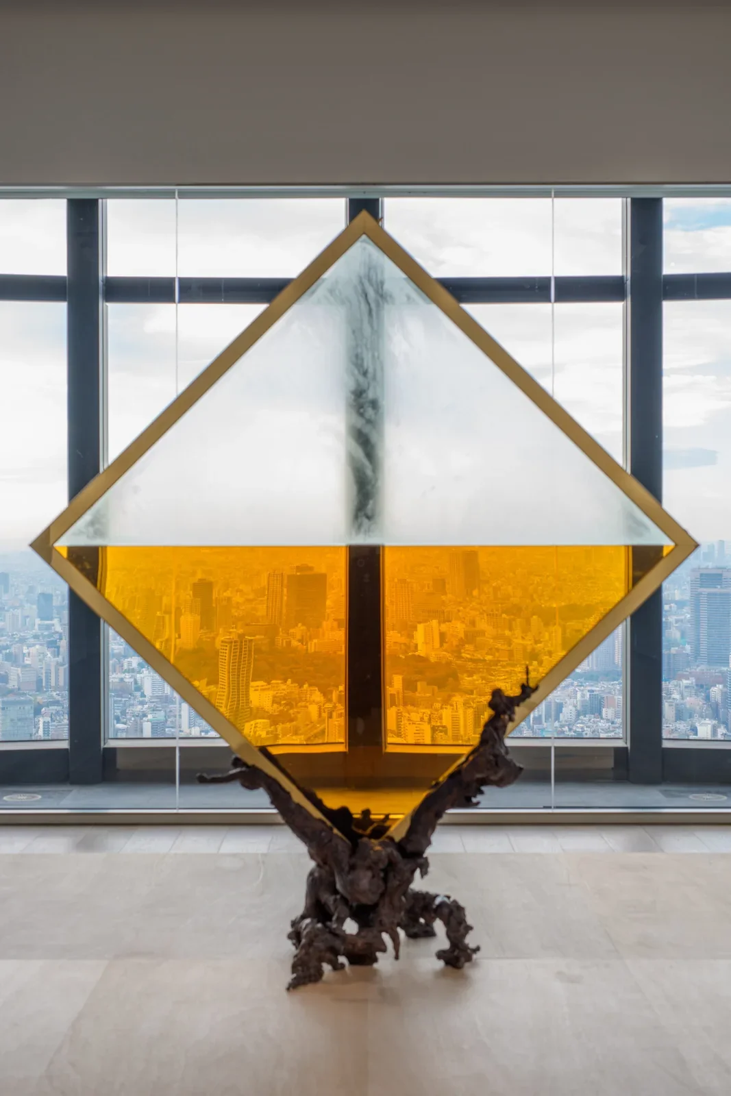 Un losange de verre partiellement rempli de brandy filtre la vue de Tokyo, posé sur un socle de bronze évoquant une vigne.