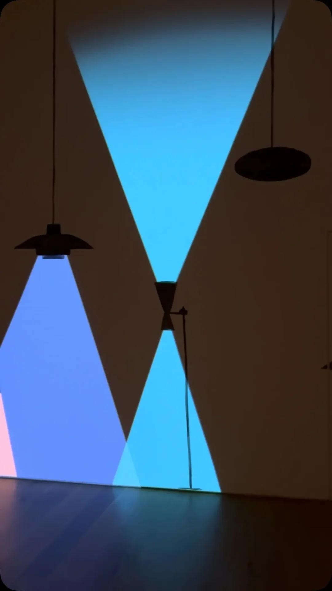 Installation vidéo et dessin de Zilla Leutenegger dans SPACES BETWEEN : faisceaux triangulaires bleus et roses projetés sur un mur.
