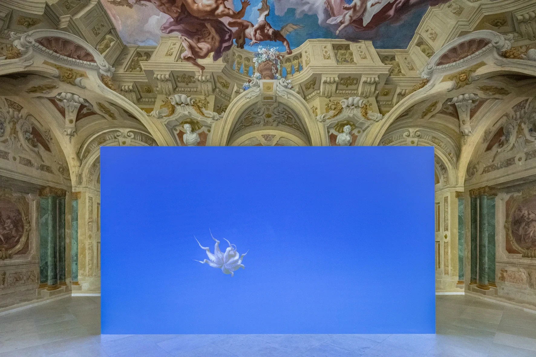 Things d’Asta Gröting : un poulpe suspendu dans un ciel bleu sur un écran devant les fresques de la salle Carlone.