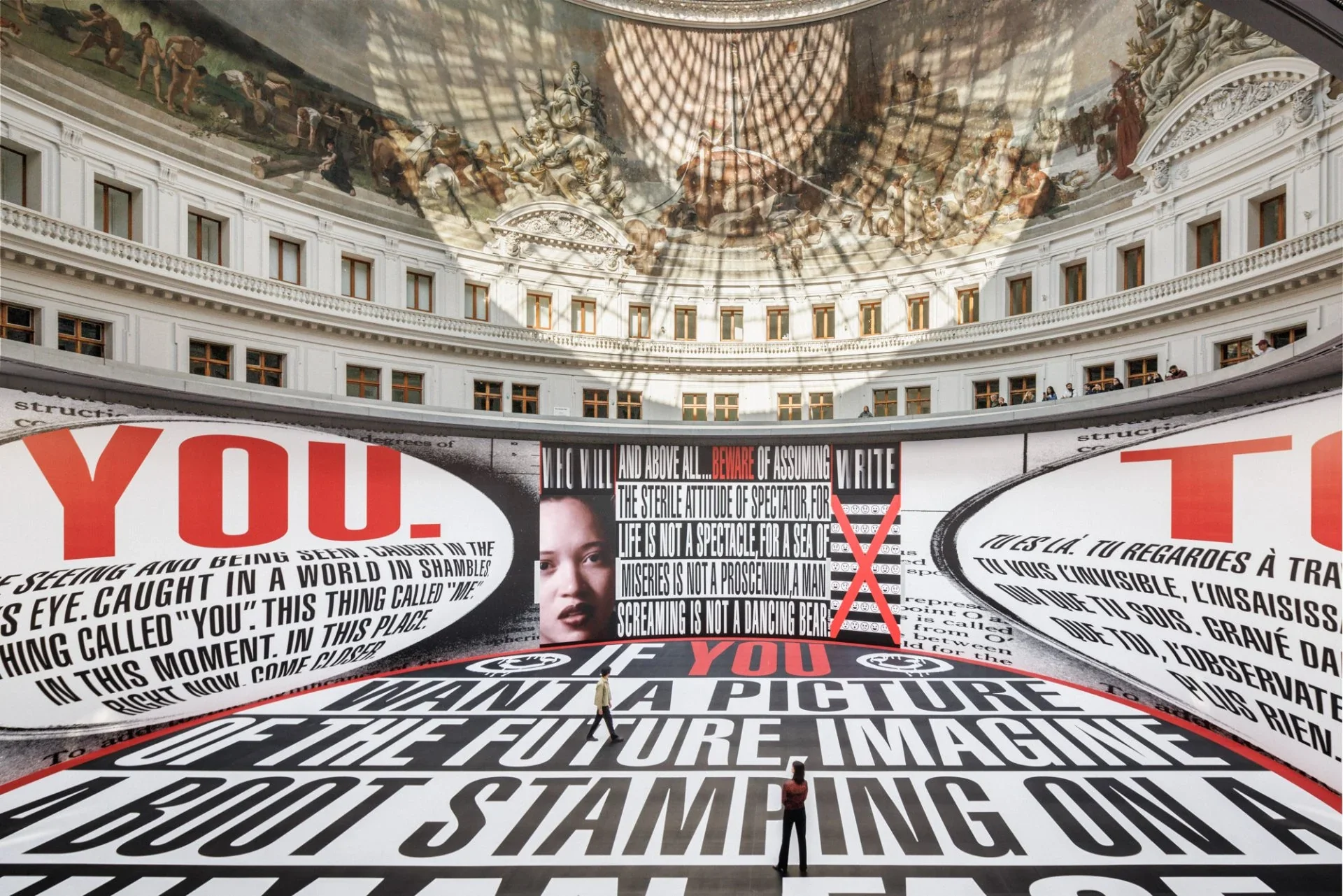 L’installation The History of Tears de Barbara Kruger recouvre le sol et les murs de la Rotonde de phrases noires, blanches et rouges ; deux visiteurs en révèlent l’échelle.