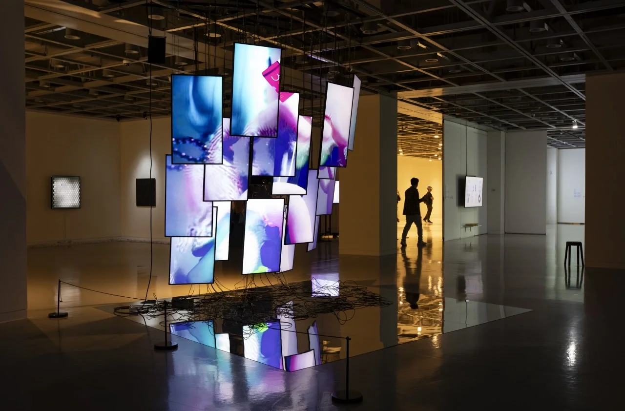 Écrans suspendus aux images numériques colorées et câbles visibles dans hard data / soft bodies.