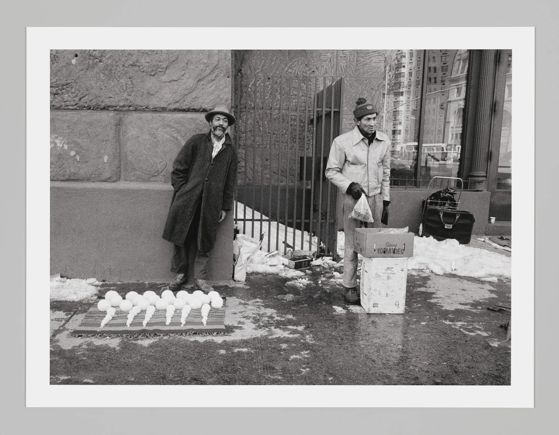 David Hammons devant des rangées de boules de neige proposées à la vente sur un trottoir de New York, photographié par Dawoud Bey.