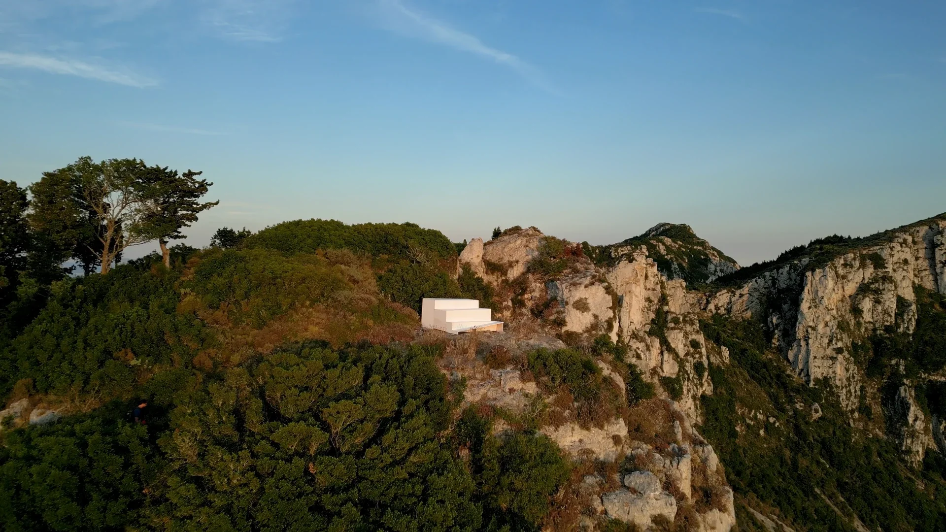 Une plateforme blanche de quatre marches sur une falaise rocheuse et boisée de l’île d’Othoni.