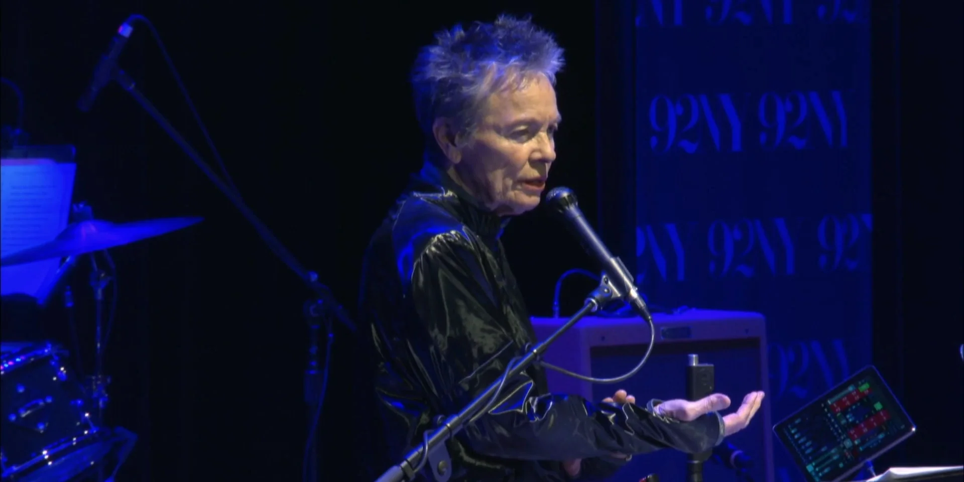 Laurie Anderson sur scène à Muldoon’s Picnic, 92NY, le 14 septembre 2026, une main ouverte devant le microphone et son matériel de performance.