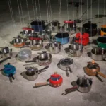 Vingt-cinq casseroles de couleurs et de formes variées, leurs couvercles reliés à des fils, dans l’installation de Michel Winterberg à E-WERK Freiburg.