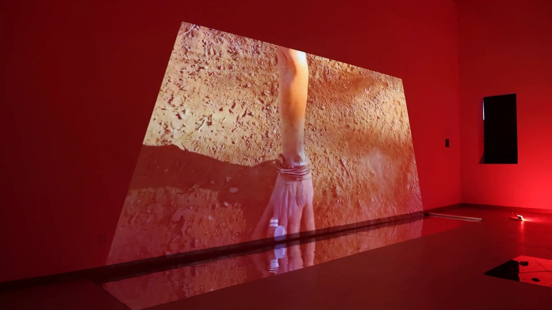 Une projection monumentale d’une main se reflète au sol dans l’espace rouge de Trapezoidal Memory, installation de Nadia Coën à KinoSaito.