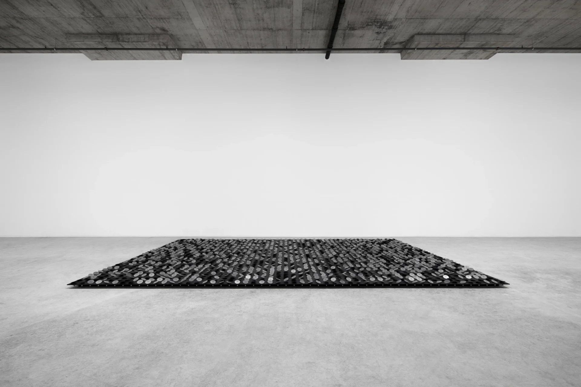 Un vaste tapis de disques métalliques motorisés sur une plateforme noire, face à un mur blanc : l’installation de Zimoun à Genève en 2020.